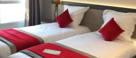 Habitación de hotel con dos camas, cada una con ropa de cama blanca y detalles rojos, cabeceros modernos, una lámpara de pared y un cuadro abstracto grande.