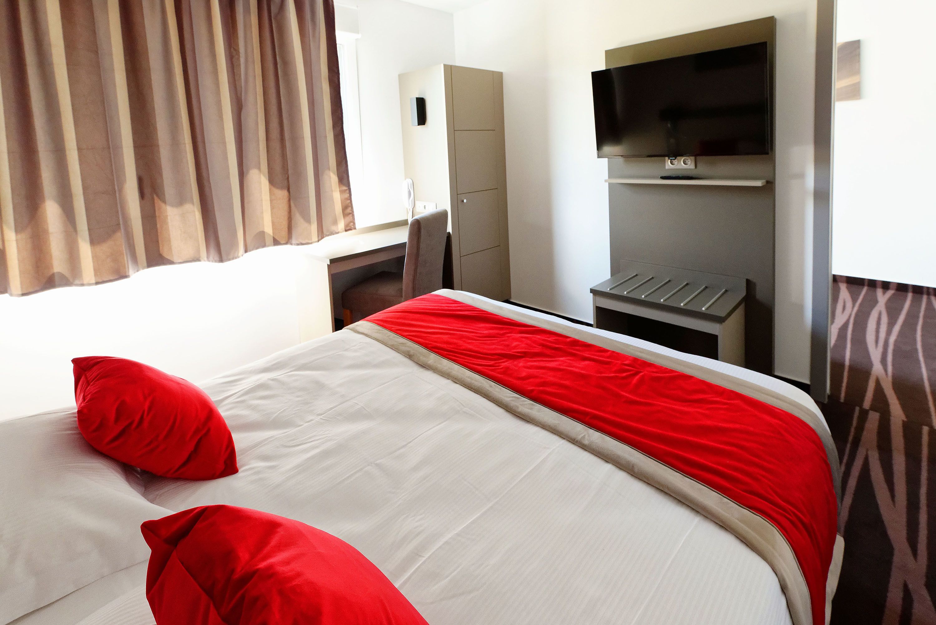 A hotel room with a bed, a desk, a wardrobe, and a television.