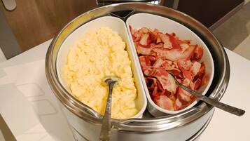 A stainless steel food container with scrambled eggs and bacon.