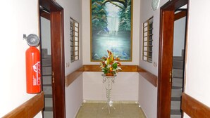 A hallway with a fire extinguisher, a painting of a waterfall, and a flower vase on a pedestal. - Residence Hotel Badjo (Abidjan)