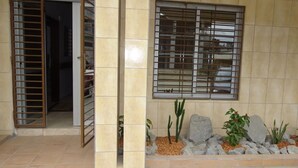 A building entrance with a metal gate, a window with bars, and a small rock garden with plants. - Residence Hotel Badjo (Abidjan)