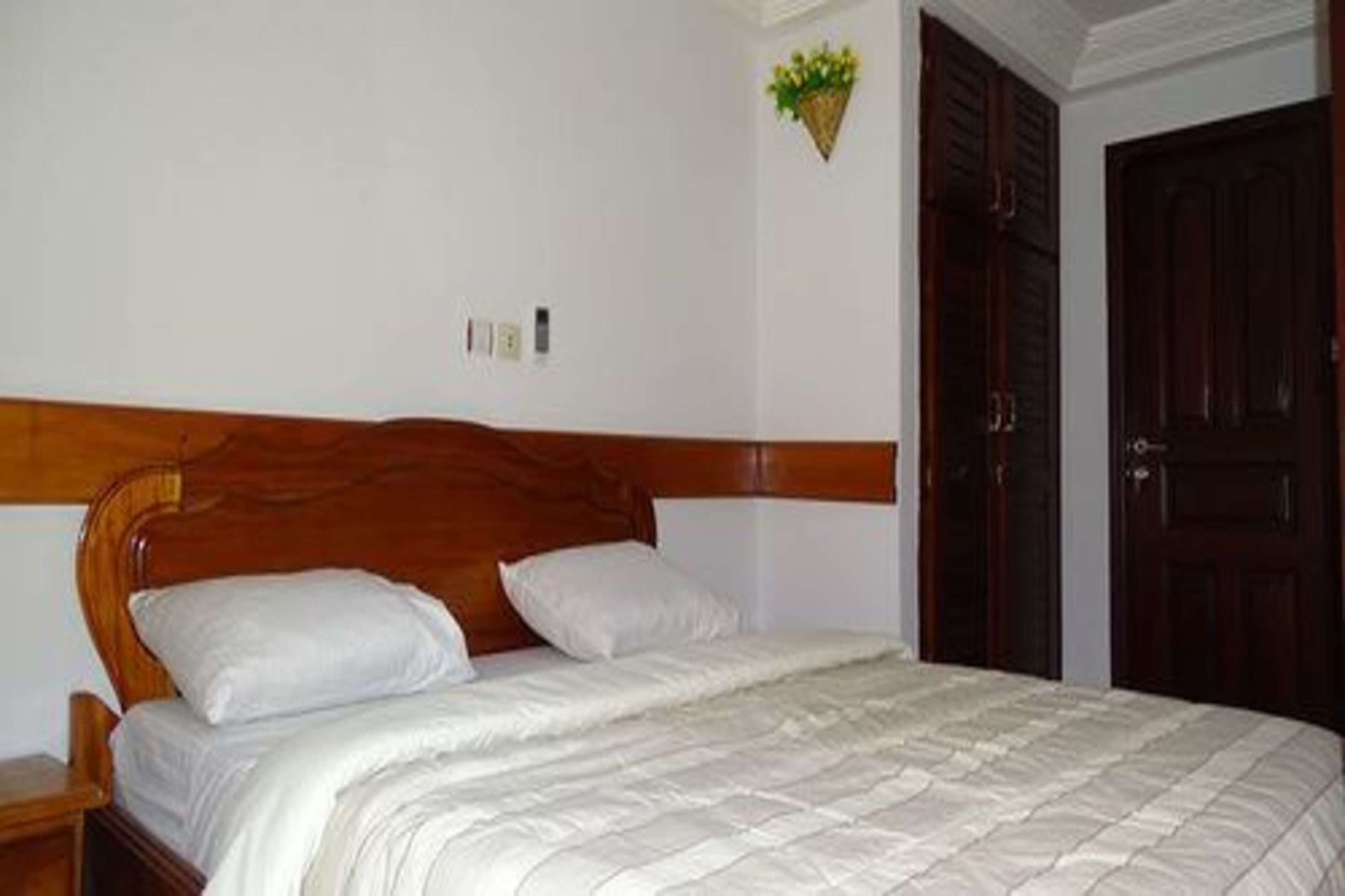 A neatly made bed with white linens, a wooden headboard, and a small bedside table.