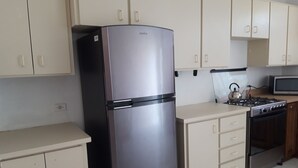 A kitchen with a stainless steel refrigerator, a stove, a microwave, and beige cabinets. - Personal Touch Studio (Nassau)
