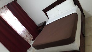 A bed with a brown mattress and white pillows, a wooden headboard, and a green rug on a tiled floor. - Personal Touch Studio (Nassau)