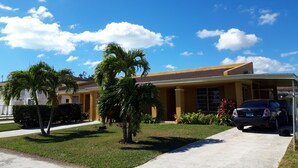 A two-story building with a yellow facade, a covered driveway, and a parked car. - Personal Touch Studio (Nassau)