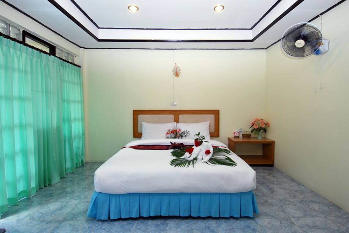 A neatly arranged bedroom with a bed, a nightstand, a fan, and a window with curtains.