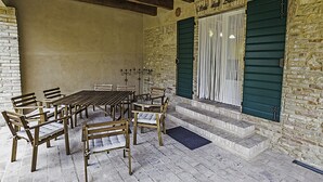 Ein überdachter Außenbereich mit Tisch und Stühlen, Steinmauern und einer Holzbalkendecke.