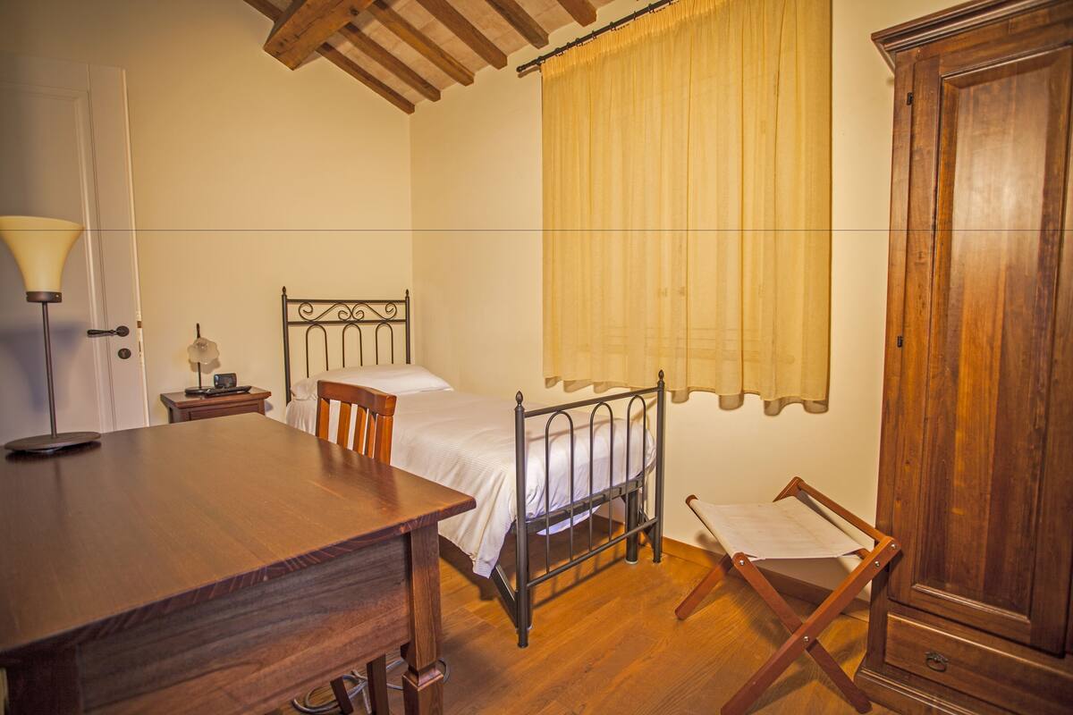 A bedroom with a wooden bed, a bedside table, a lamp, a wooden wardrobe, and a window with curtains.