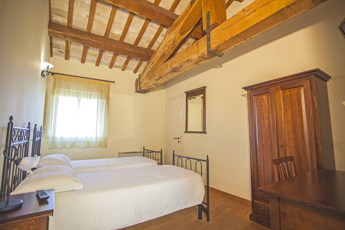 A bedroom with two beds, a wooden wardrobe, a mirror, and a window with curtains.