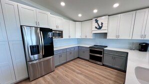A modern kitchen with white cabinets, stainless steel appliances, and a wooden floor.