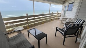 A covered outdoor area with a view of the ocean, featuring a table, chairs, and a small round table.