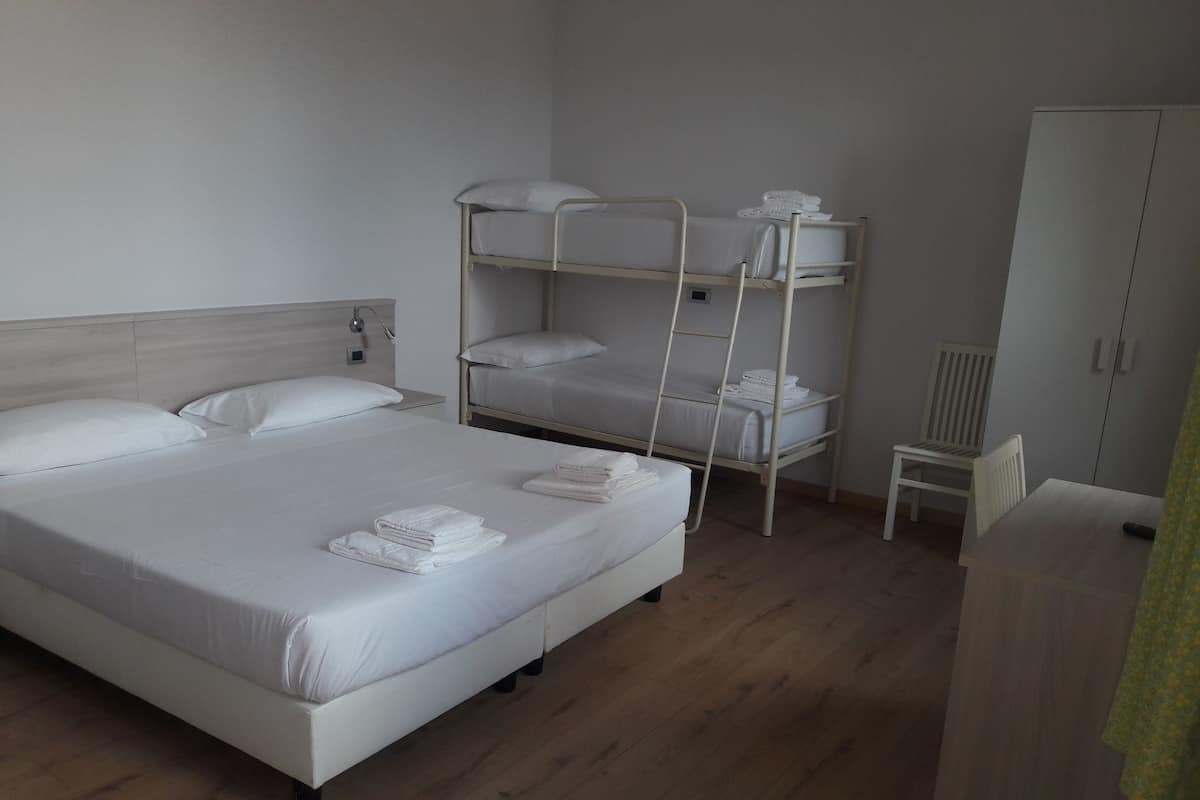 Ein Hotelzimmer mit einem Einzelbett, einem Etagenbett, einem Holzschrank und einem kleinen Tisch.