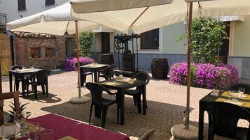 Ein Terrassenbereich im Freien mit Tischen und Stühlen unter Sonnenschirmen, umgeben von Backsteinmauern und blühenden Pflanzen.