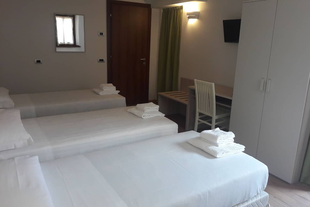 Ein Hotelzimmer mit zwei Einzelbetten, einem Schreibtisch, einem Stuhl, einem Kleiderschrank und einem Fernseher.