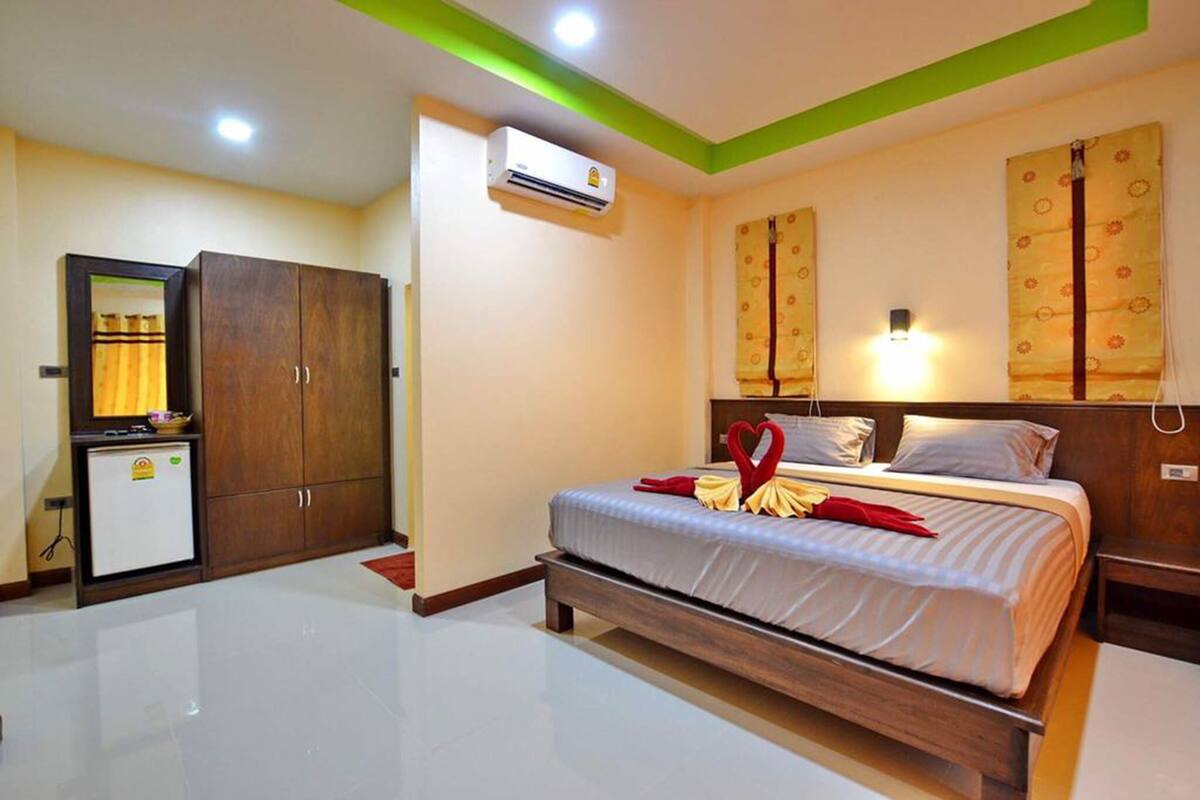 A hotel room with a bed, a wardrobe, a desk, and an air conditioning unit.