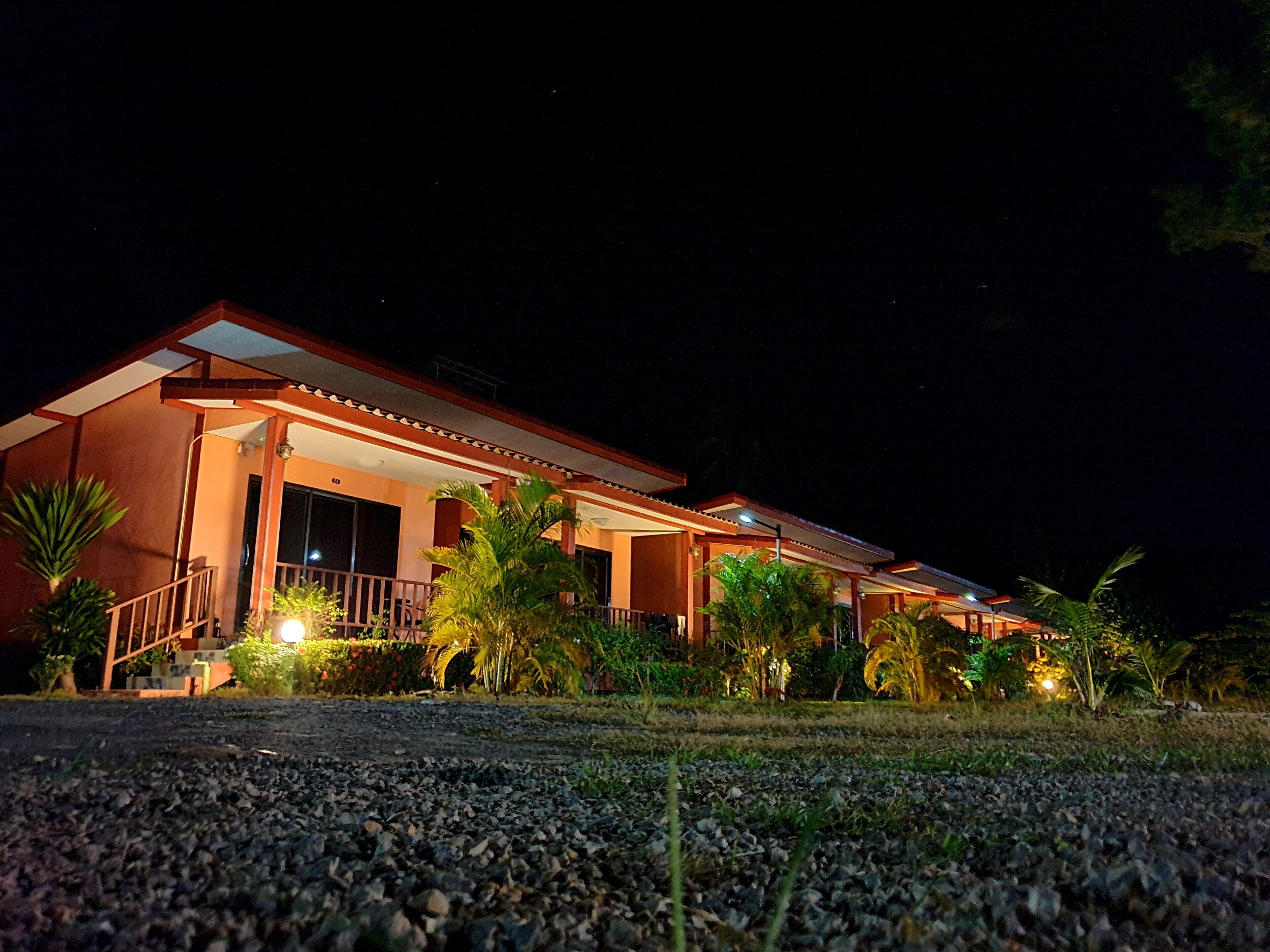 A two-story building with a balcony and a covered walkway, surrounded by greenery.