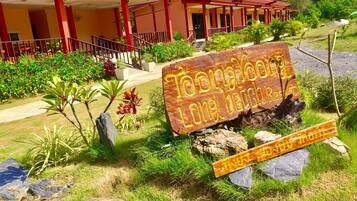 A wooden sign with the text "Toonghoo Long Beach Resort" in front of a building with a red roof and multiple balconies.