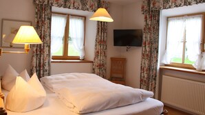 Una cama bien hecha con sábanas blancas, una lámpara de noche y cortinas florales en una ventana.