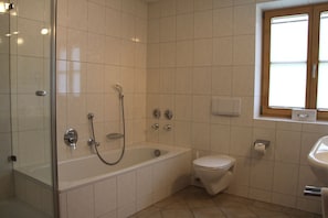 A bathroom with a bathtub, toilet, and a window.