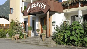 Un hôtel avec une enseigne indiquant « HÔTEL RESTAURANT CAFÉ HUBERTUS » et des balcons ornés de jardinières fleuries.