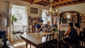 Une salle à manger avec une table et des chaises en bois, un lustre et une fenêtre avec des rideaux.