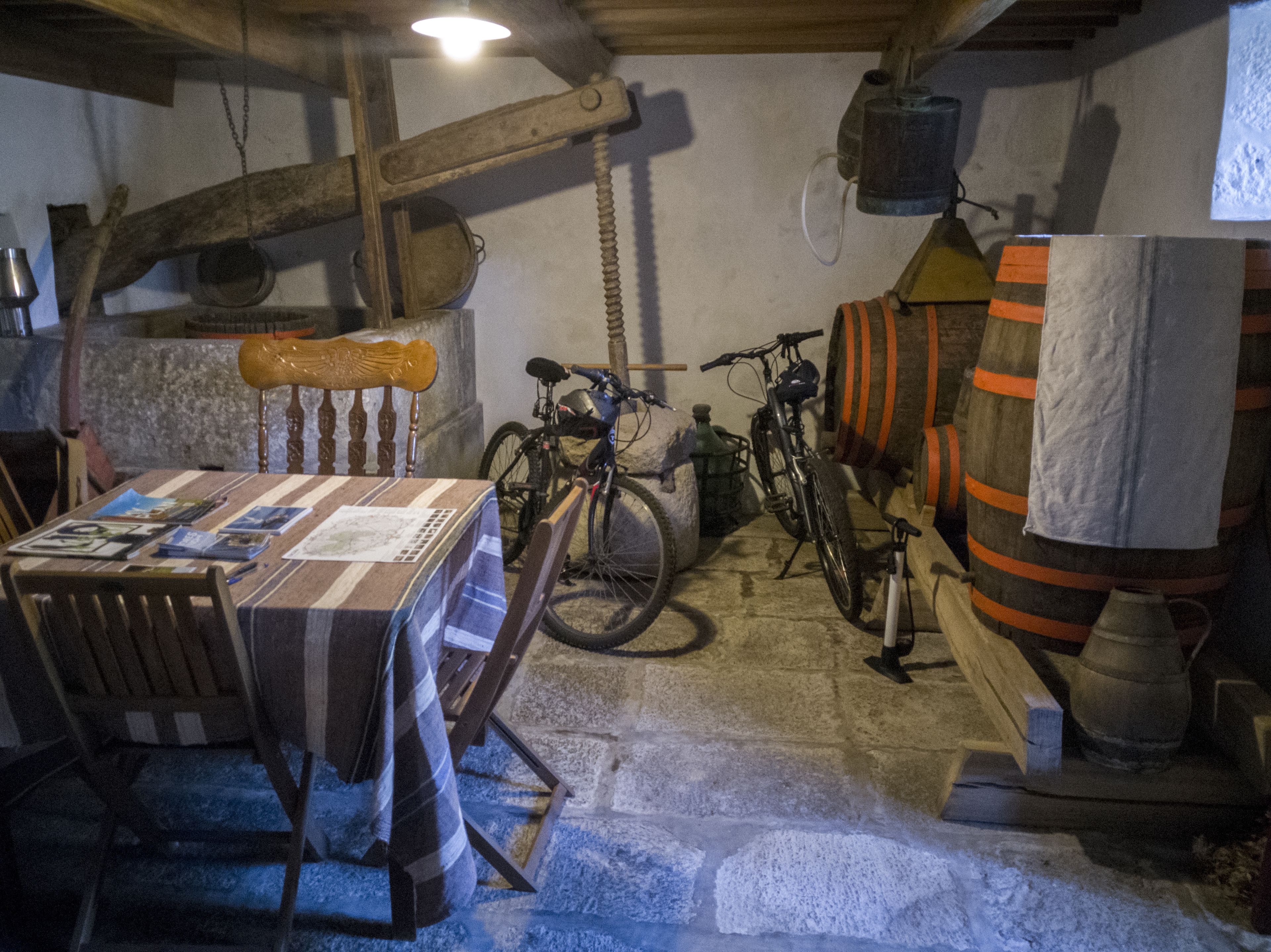 A rustic room with a wooden table, chairs, bicycles, and a barrel.