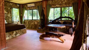 Um quarto com paredes de pedra, lareira de pedra, sofá, mesa de jantar e um cão deitado no chão.