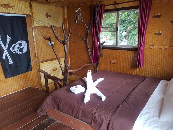 A wooden room with a bed, a chair, a window with curtains, and a wall with a skull and crossbones flag.