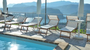 Zona junto a la piscina con sillones de descanso y sombrillas, con vistas a un paisaje montañoso.