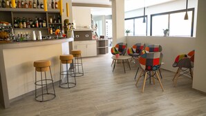 Una cocina moderna con taburetes, una zona de comedor con sillas coloridas y una barra provista de diversas botellas.
