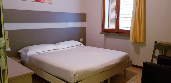 A single bed with a headboard, a bedside table, a chair, and a window with blinds. - Hotel Stampa 1968 (Cadegliano-Viconago)
