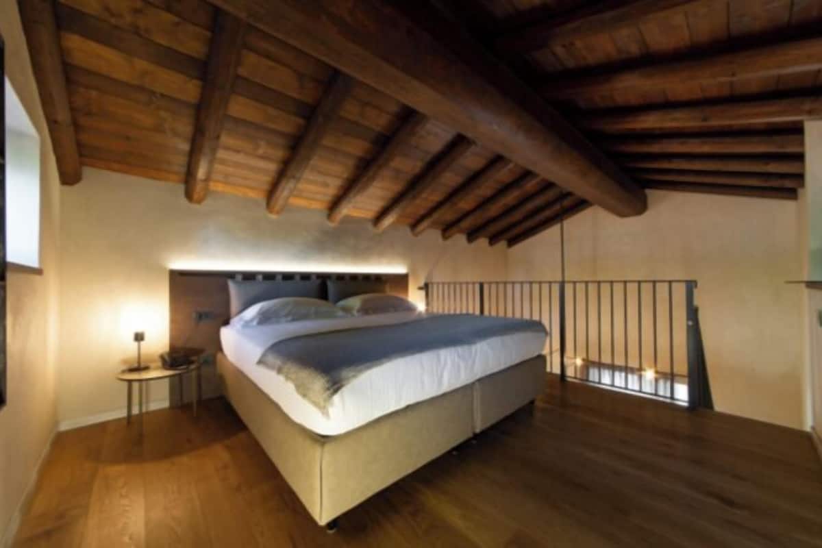 A bedroom with a wooden ceiling, a bed with a headboard, a nightstand, and a small table.