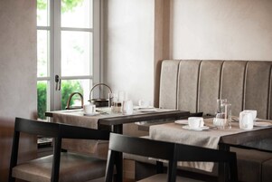 Zona pranzo con tavolo imbandito per due persone, una panca imbottita e vista su piante.