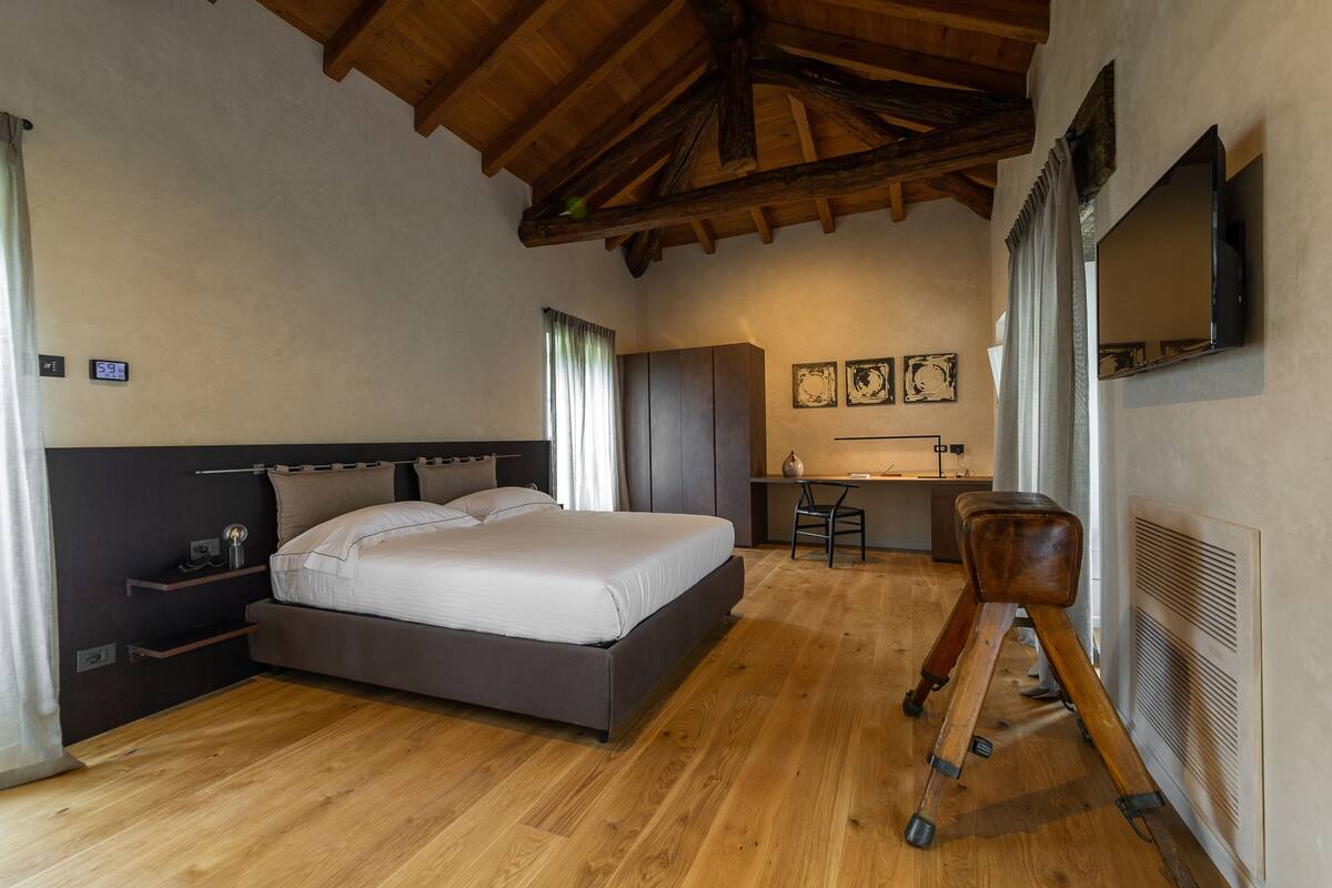 A bedroom with a large bed, wooden flooring, a desk, and a chair.