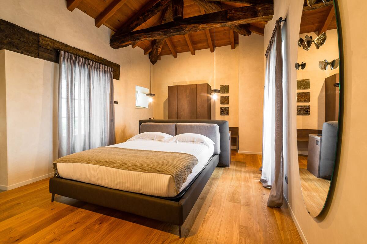 A bedroom with a wooden floor, a bed with a headboard, a wardrobe, and a mirror.