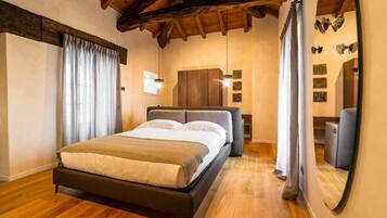 A bedroom with a wooden floor, a bed with a headboard, a wardrobe, and a mirror.