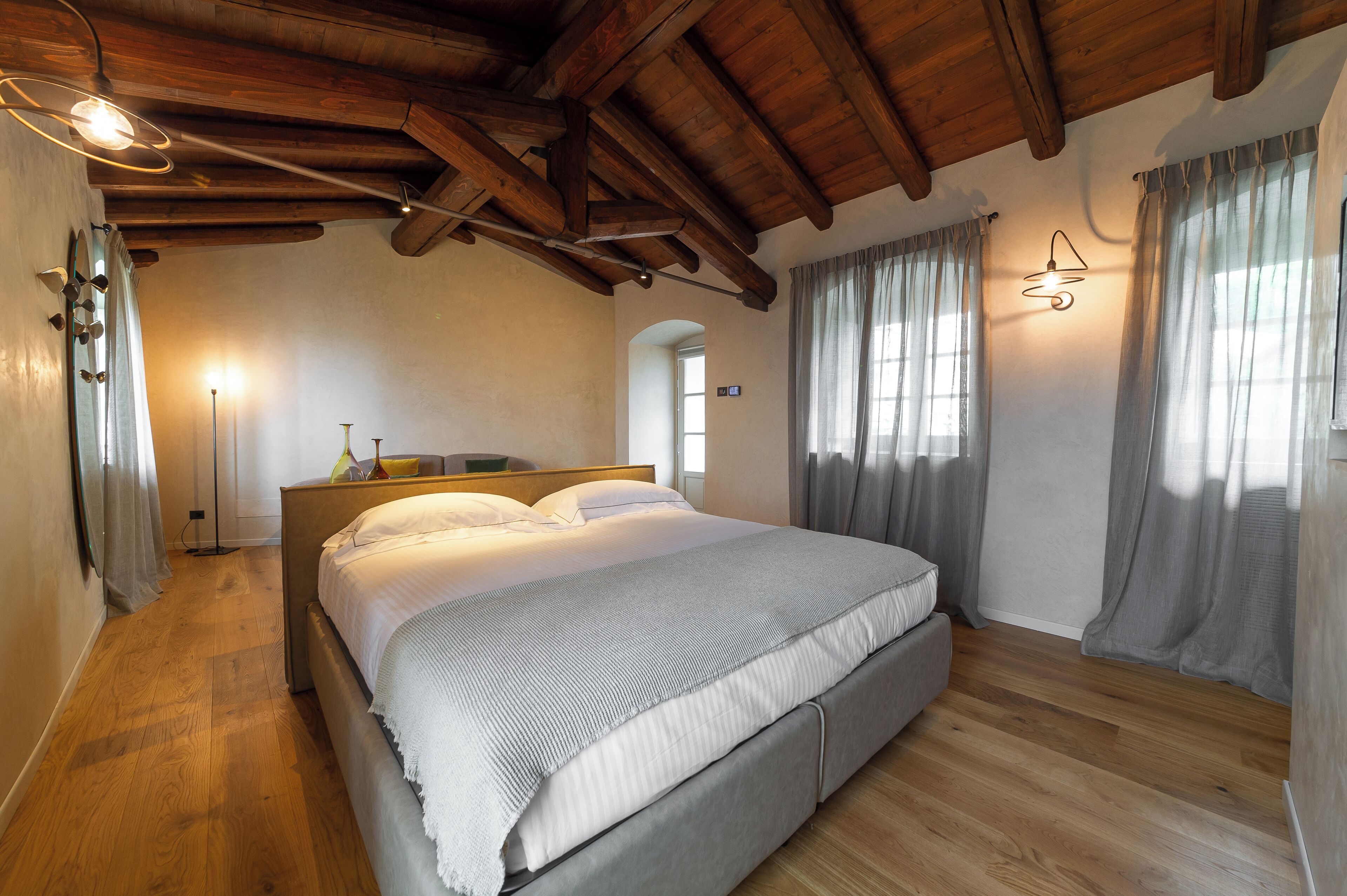 Une chambre avec un plafond en bois, un lit avec une literie blanche, une table de chevet et une lampe sur pied.