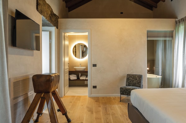 Ein Schlafzimmer mit einem Bett, einem Sessel, einem Schreibtisch, einem Spiegel und einem Badezimmer mit Waschbecken und Spiegel.