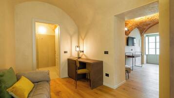 Un interior moderno con suelo de madera, un escritorio con una silla, un sofá con cojines y un televisor montado en la pared.