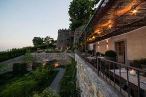A courtyard with stone walls, a dining area with tables and chairs, and a castle-like structure in the background. - Relais San Vigilio al Castello (Bergamo)
