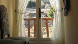 Ein Zimmer mit einer Holzbank, einer mit Vorhängen versehenen Tür und Blick auf einen Fluss und Berge.