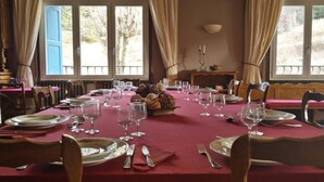Ein Esszimmer mit gedecktem Tisch, Stühlen und Blick ins Freie durch große Fenster.