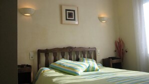 Ein Schlafzimmer mit hölzernem Kopfteil, zwei Nachttischen, einem Bett mit gestreifter Bettwäsche, zwei Wandlampen und einem gerahmten Bild an der Wand.