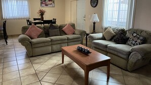 A living room with two sofas, a wooden coffee table, a dining table with chairs, a wall clock, and an air conditioning unit. - Casa Flores & Flores (Ensenada)