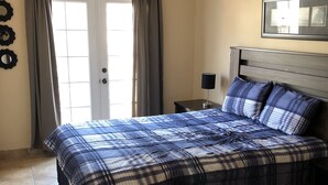 A bedroom with a bed, curtains, a nightstand, a lamp, and a framed picture on the wall. - Casa Flores & Flores (Ensenada)