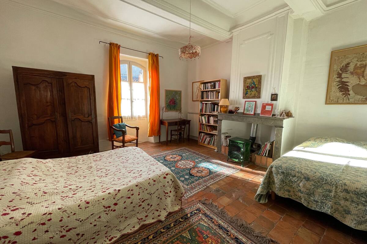 A traditional room with two beds, a wooden wardrobe, a bookshelf, and a fireplace.