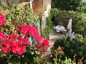 Un patio jardín con mesa y sillas, rodeado de abundante vegetación y plantas en flor.