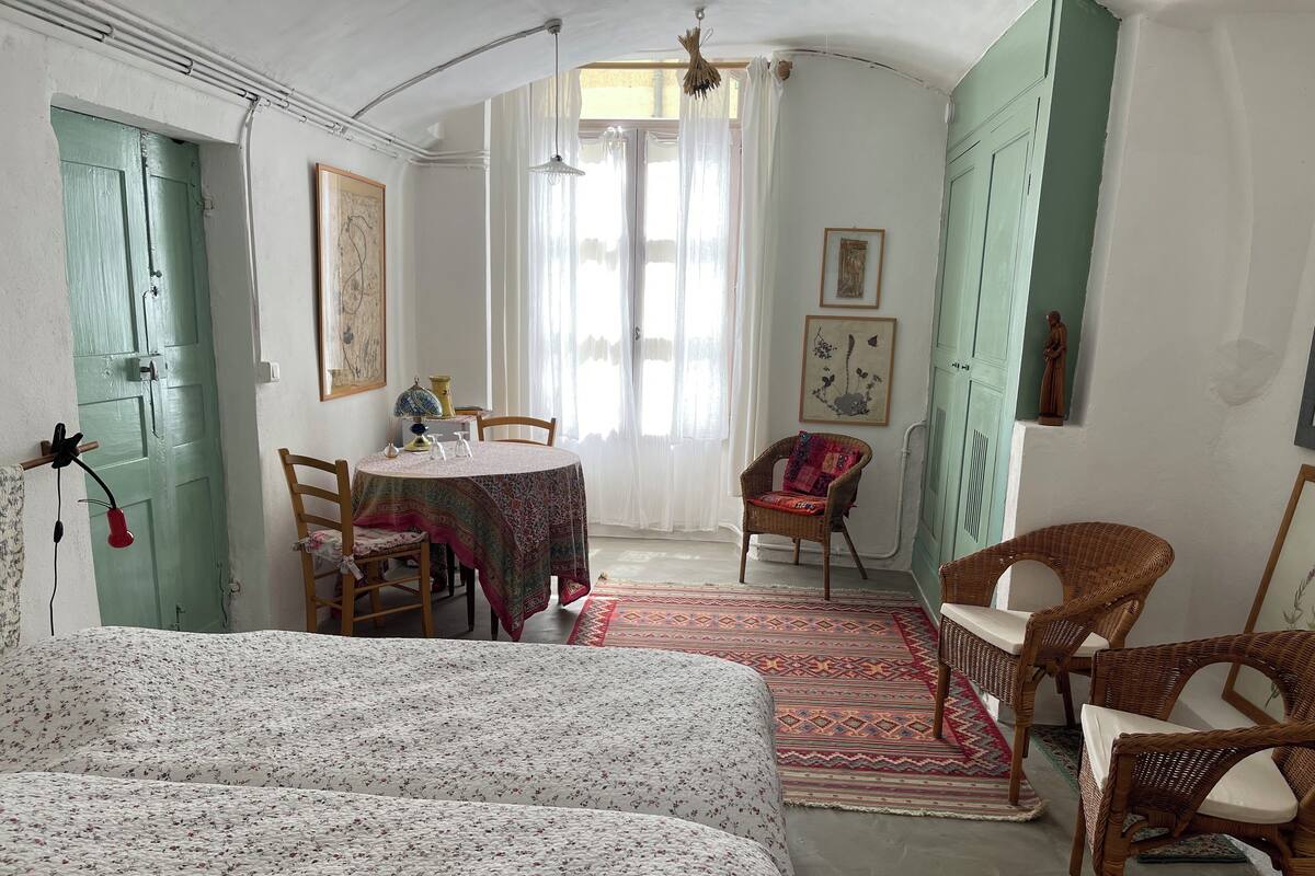 A room with a bed, a dining table, wicker chairs, and a patterned rug.