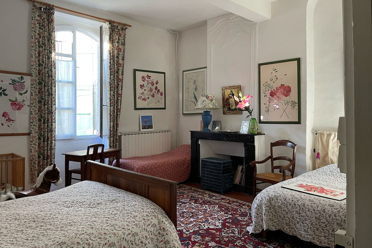 A bedroom with two beds, a wooden chair, a small table, and a radiator.