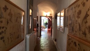 A narrow hallway with a brick floor, flanked by walls with floral patterns. There is a radiator on the left and a door leading to another room. - Les Asphodeles (Saint-Hippolyte-du-Fort)